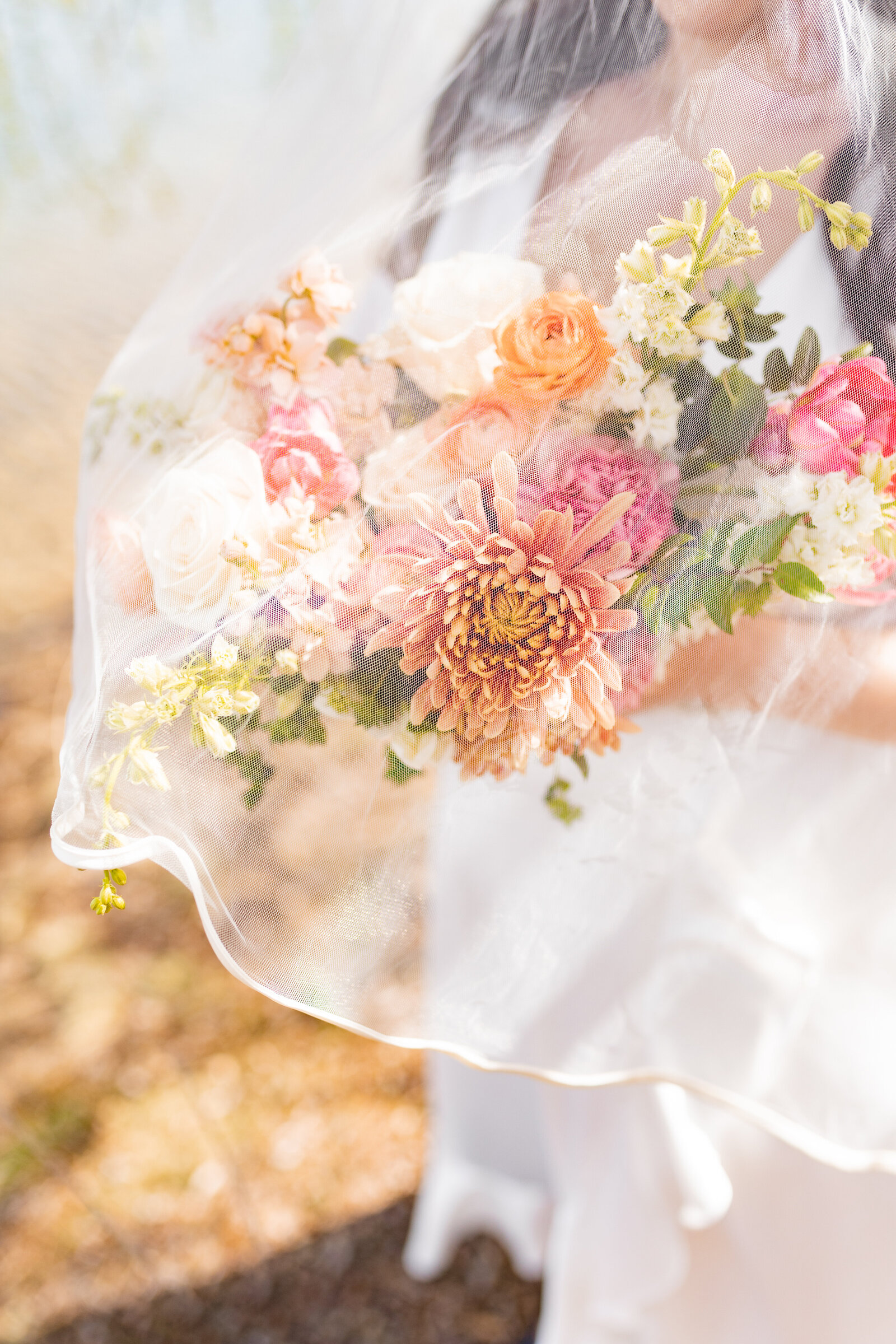 bride holding bouquet of pink and peach flowers under veil