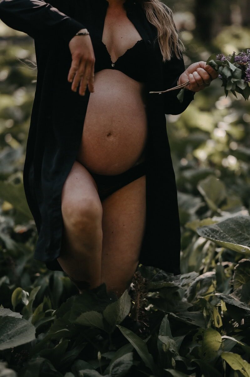 Gravid kvinna har öppen klänning gåendes i grönt gräs och växande magen blottas.