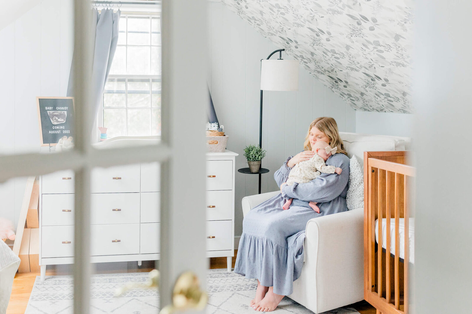 view through a french door of a mom rocking her baby to sleep in the nursery