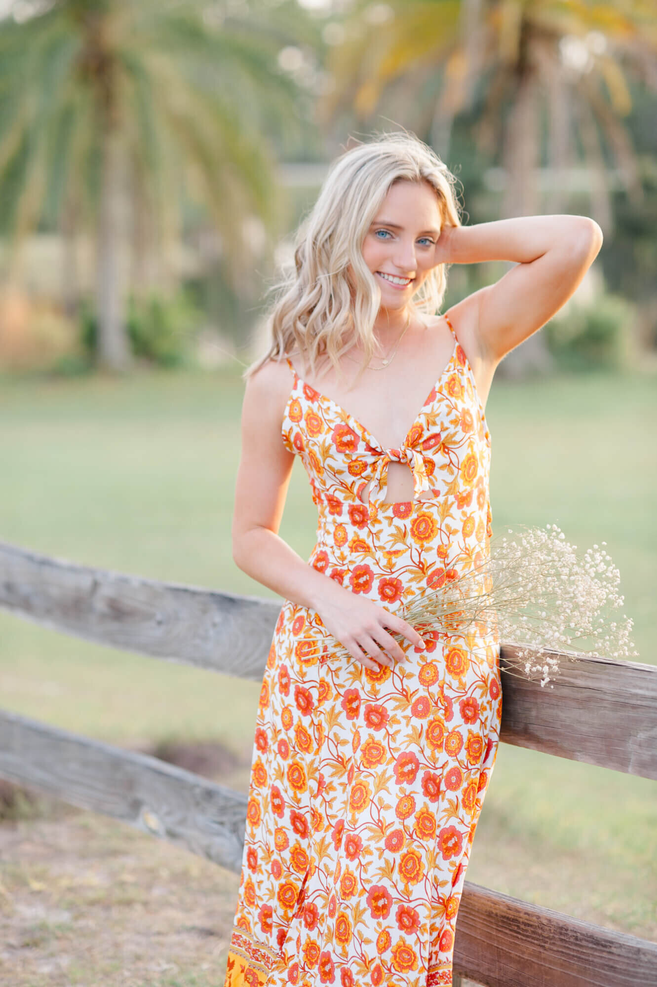Blonde senior girl stands near a fence holding babys breath during her senior photo session
