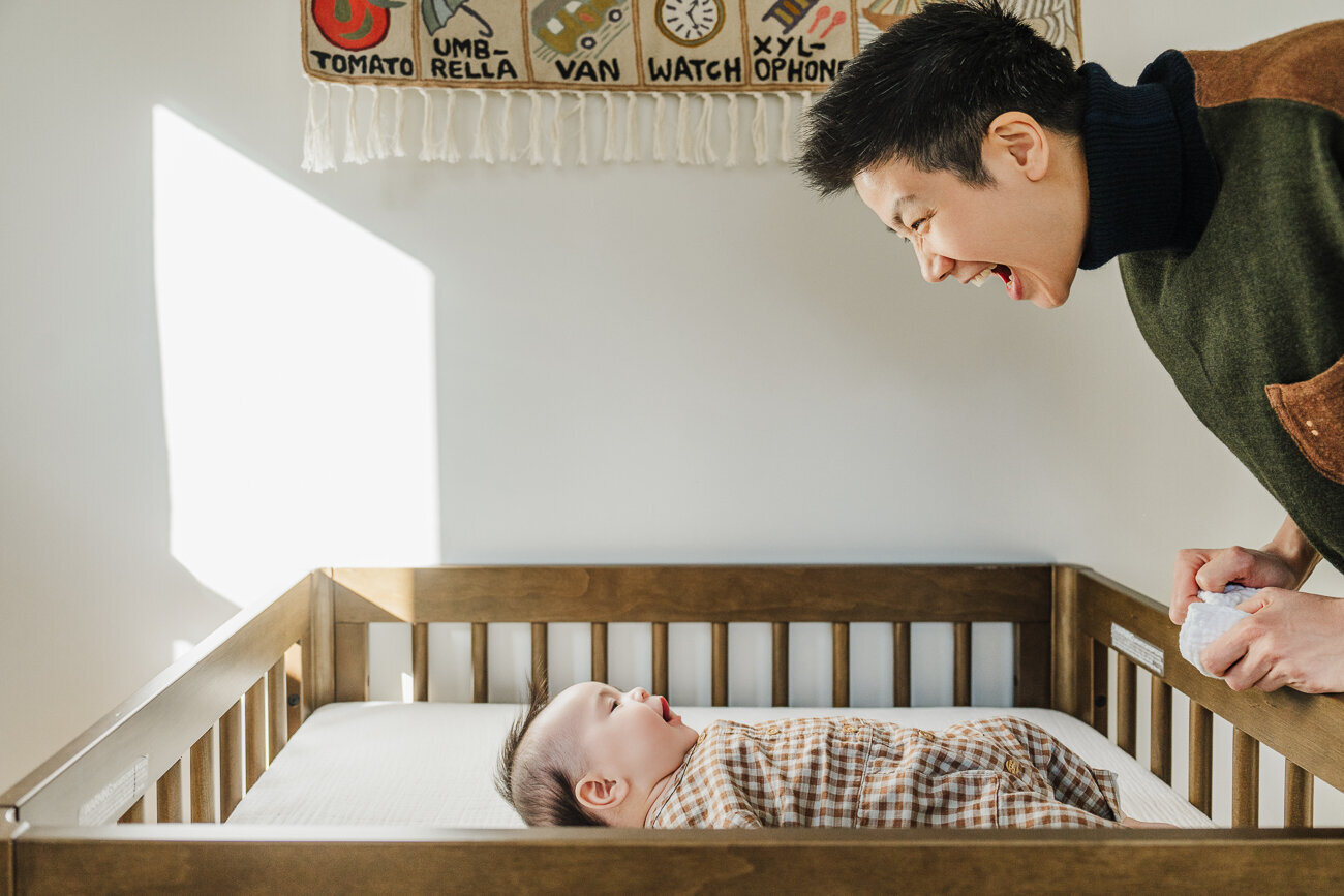mom smiles down at new baby laying in crib
