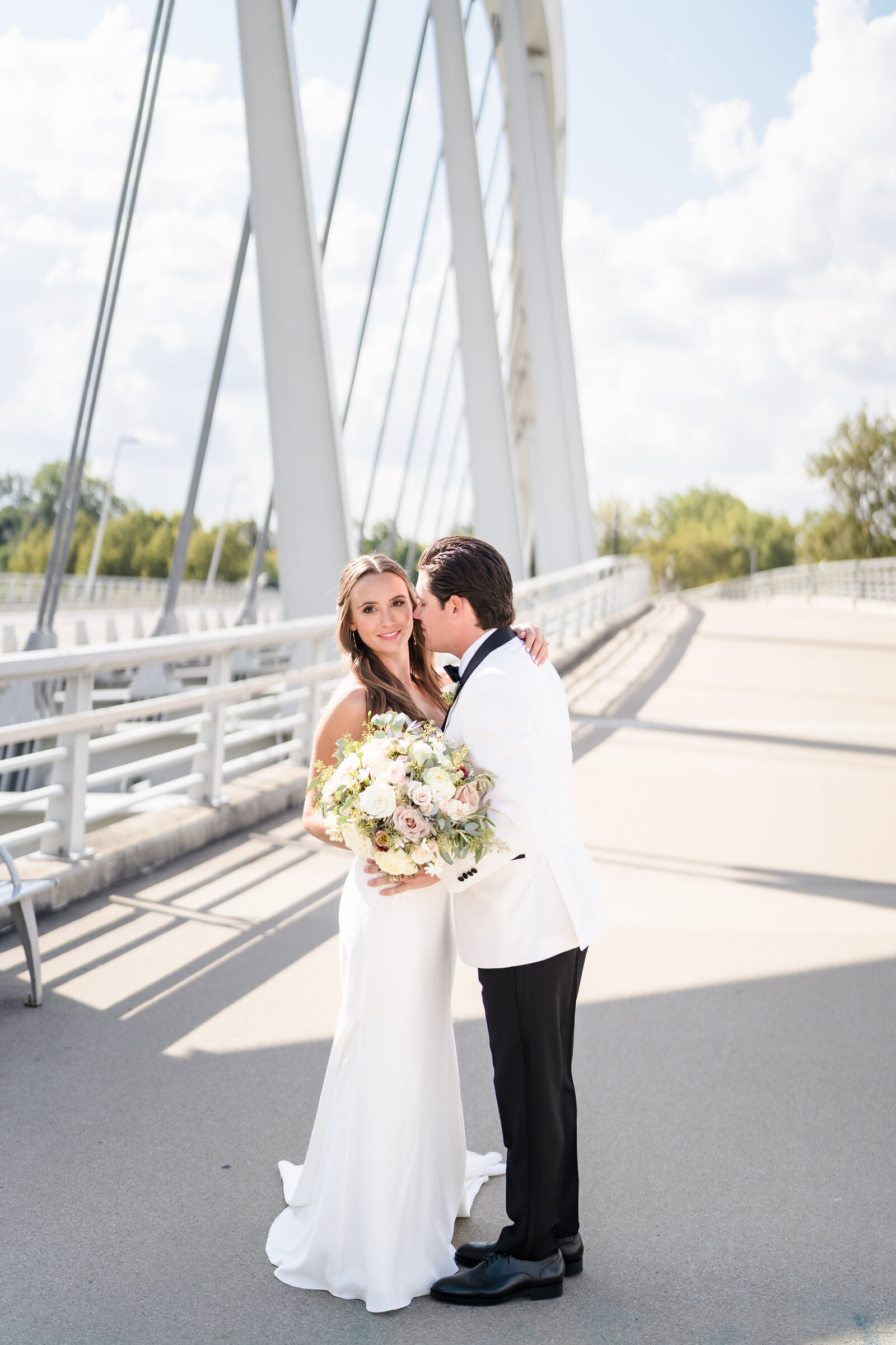 Groom leans in and whispers in his bride's ear as they stand on the Main Street Bridge