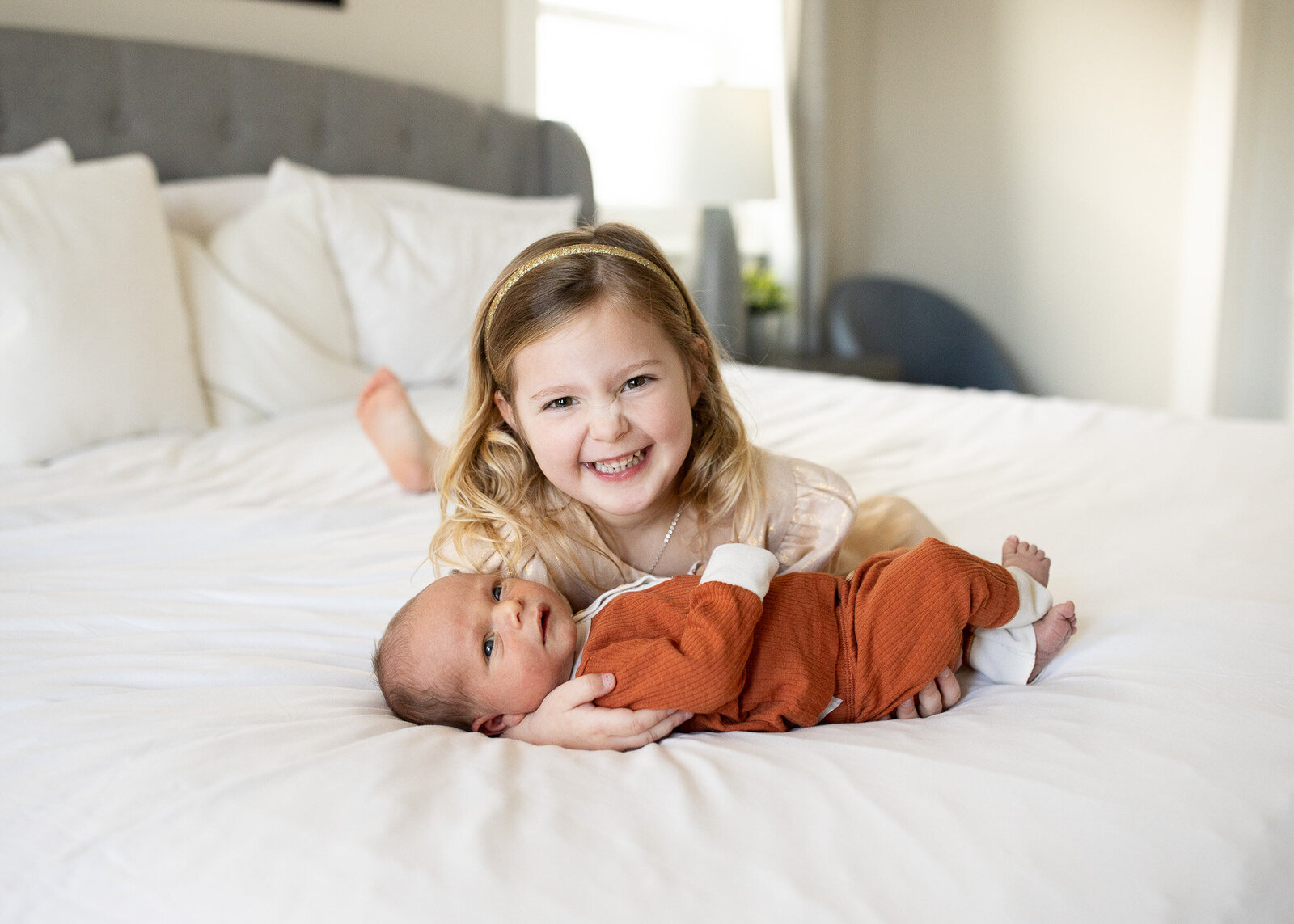 Little girl smiling with newborn brother on bed.