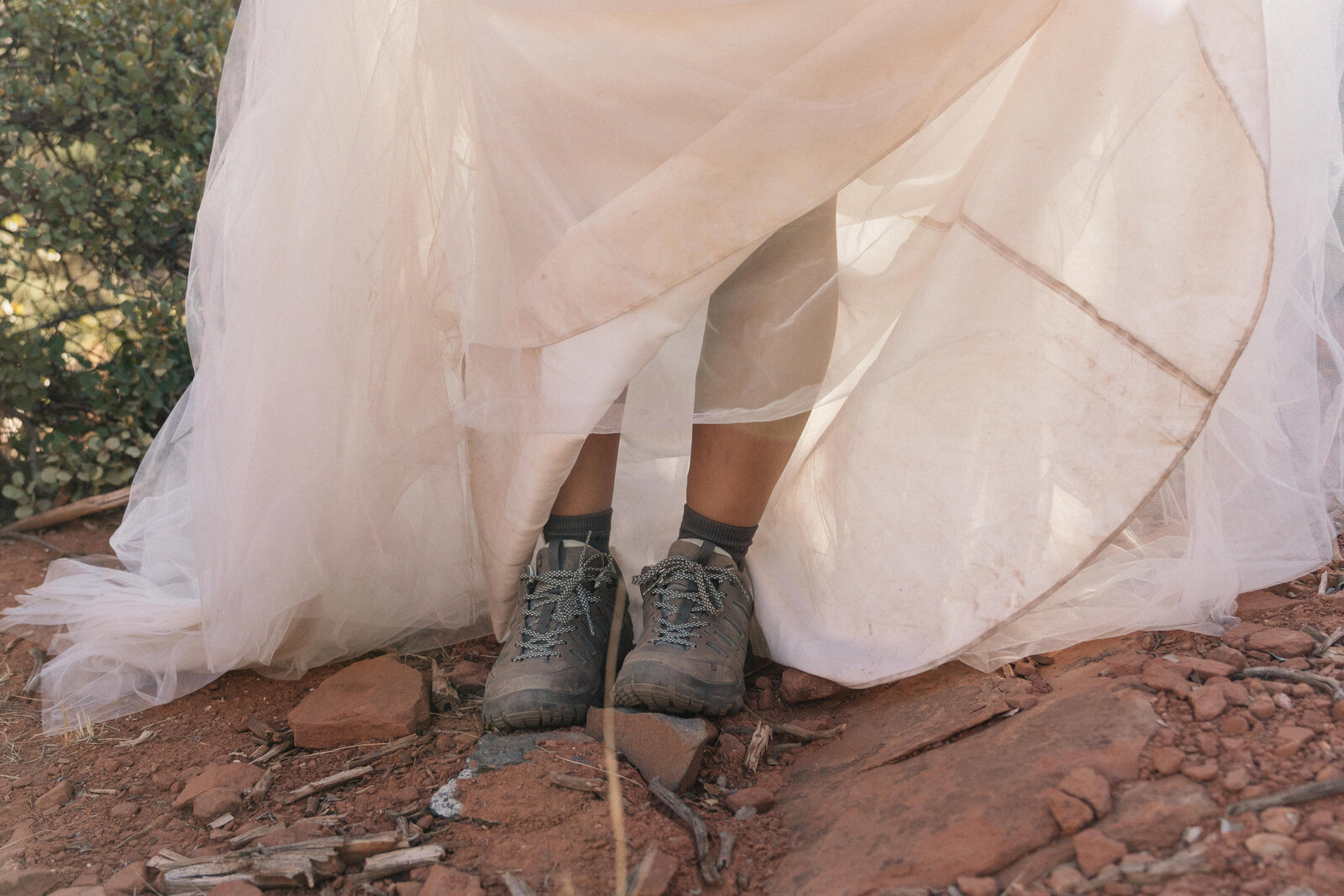 Close-up of a bride wearing hiking boots under her wedding dress on the red rock trail at Merry-Go-Round Rock during an adventurous Sedona elopement.