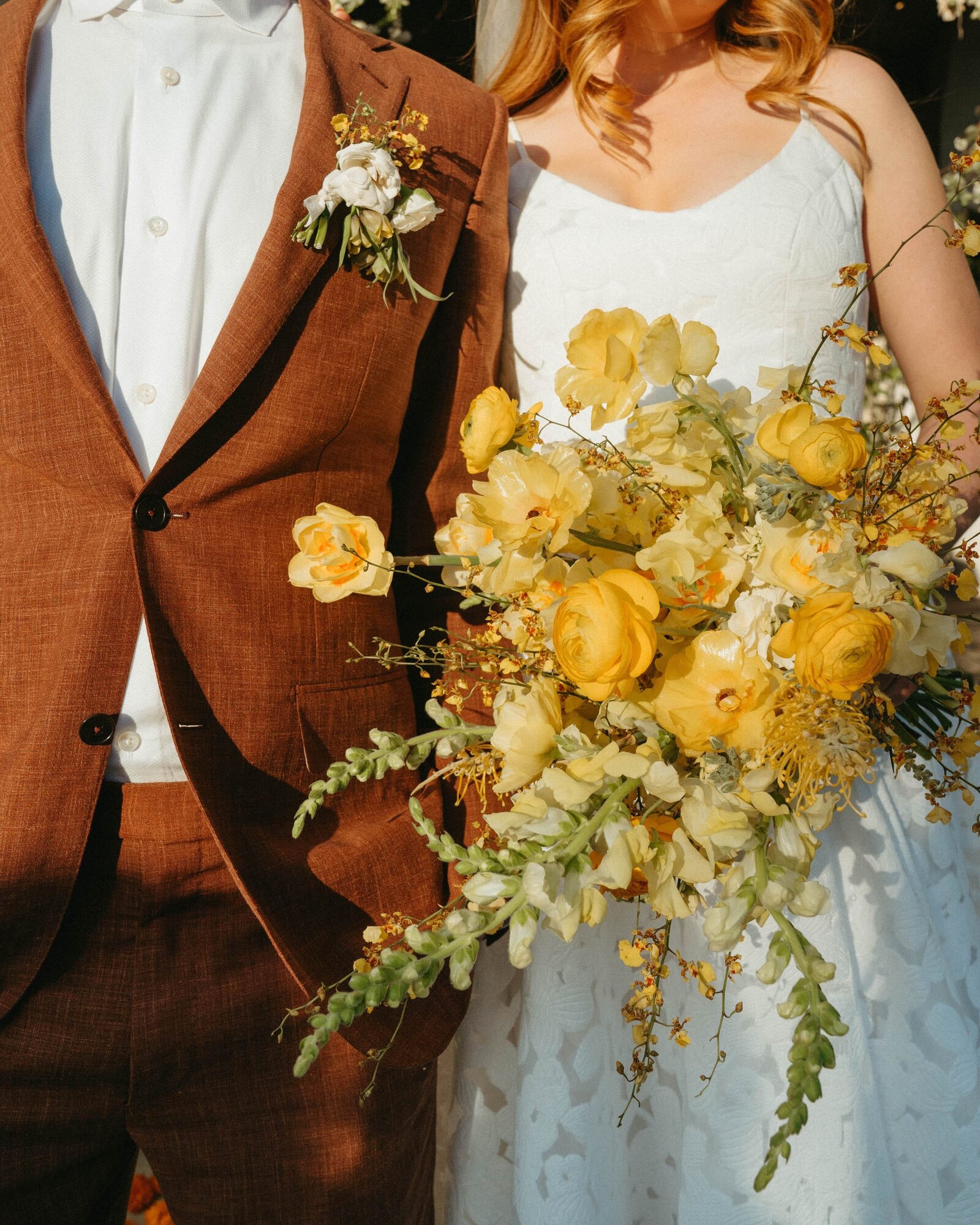 A large, all yellow bouquet is held by a bride next to her groom.
