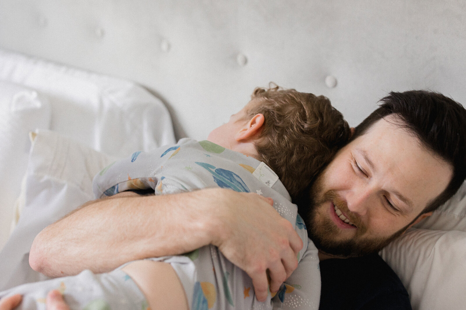 Dad hugs son in bed while they both lay in their pajamas
