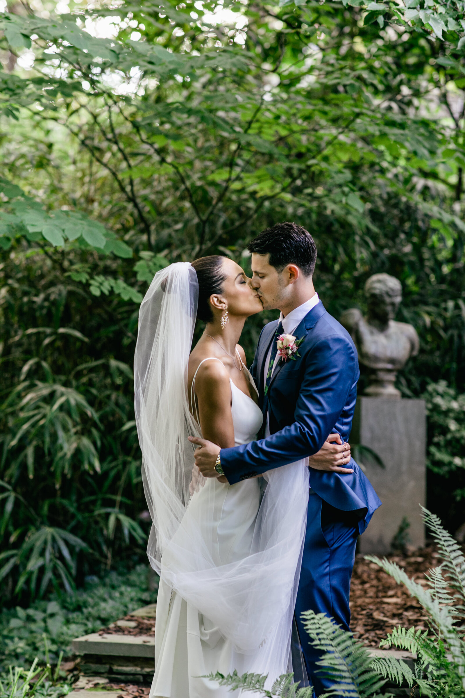 bride and groom kissing in garden sculpture