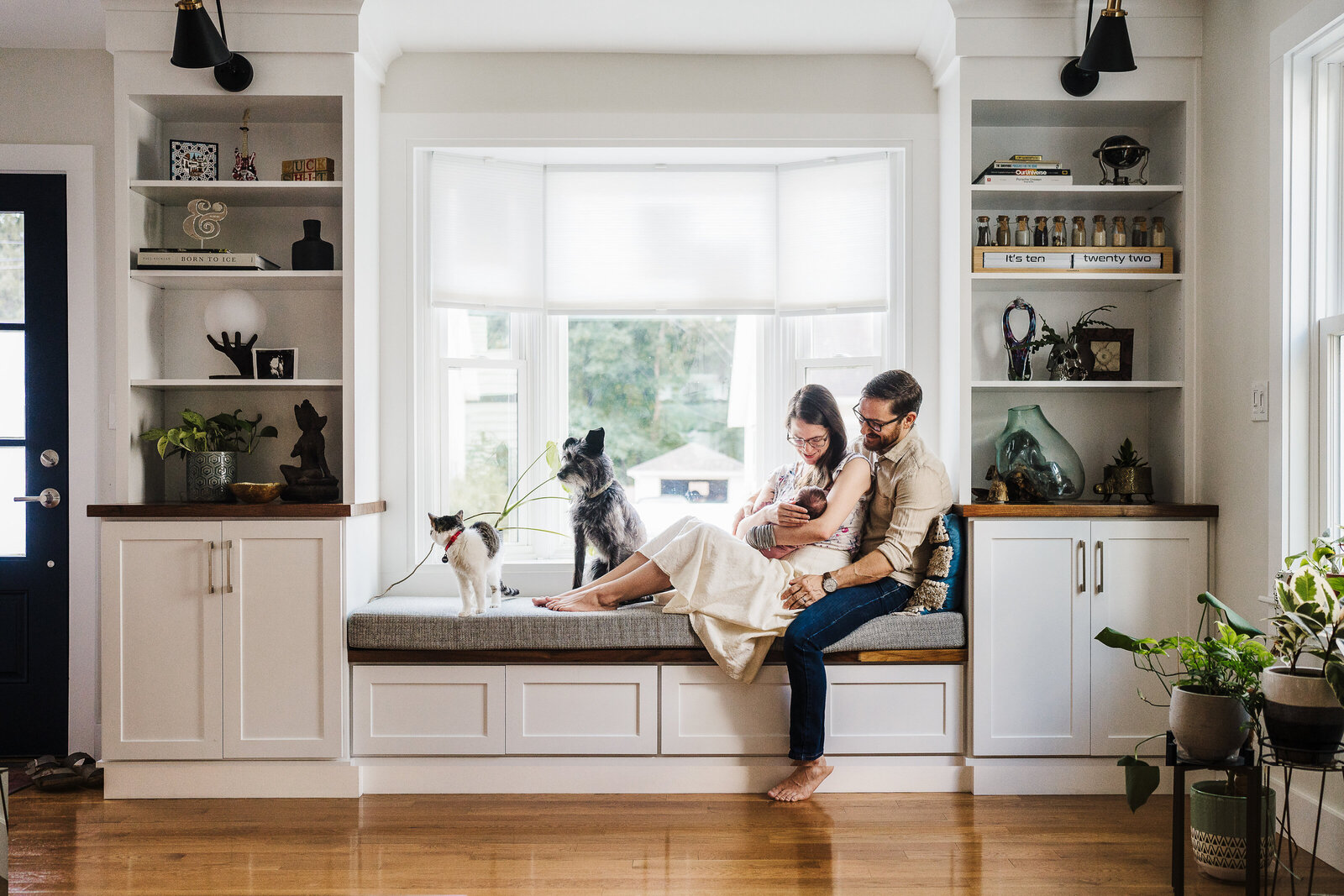 parents hold a new baby in window seat with dog and cat