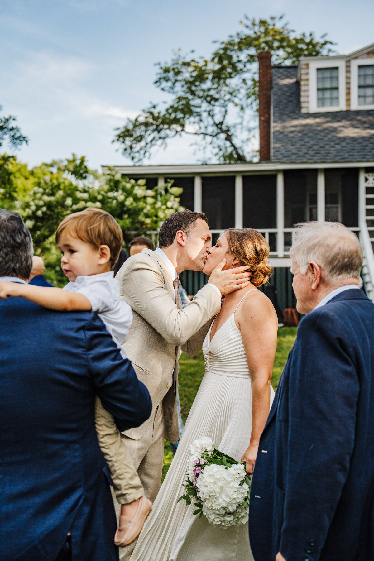bride and groom kiss amongst a crowd of family members in cottage backyard