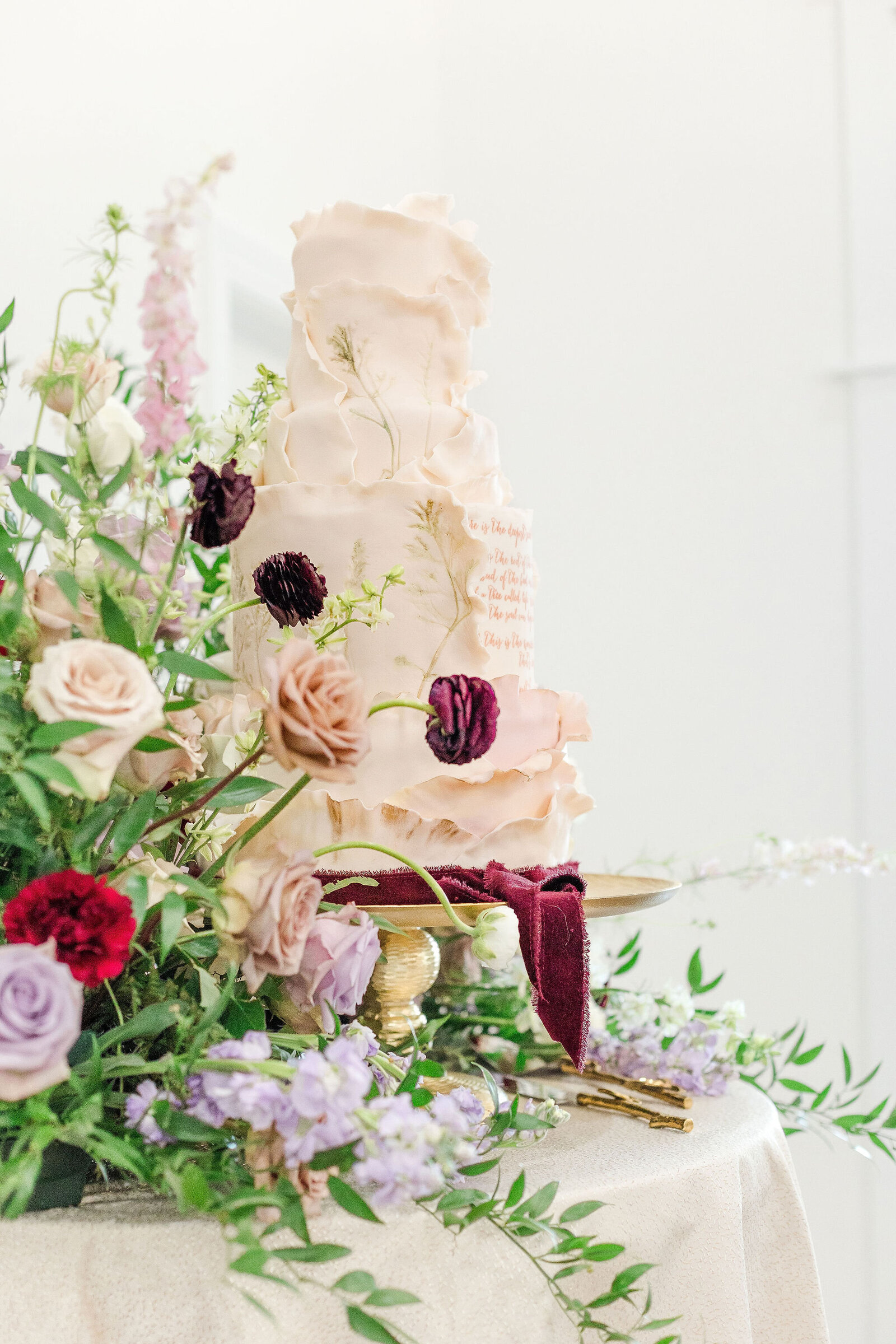 Ornate wedding cake adorned with pink and purple florals, designed by Artsy Cakesy at Willow and Stone Events in Mocksville, NC.
