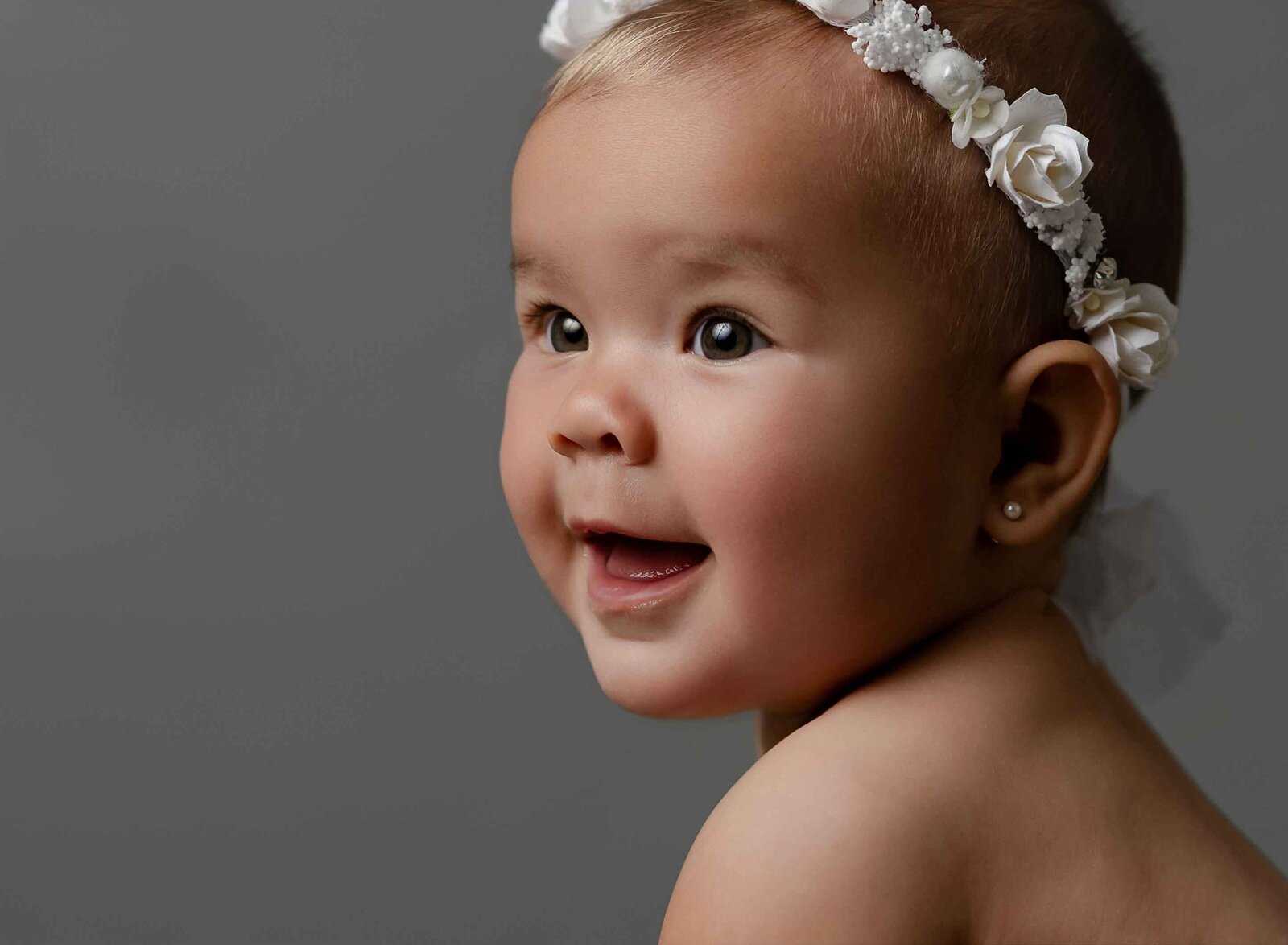 6 month baby girl sitting up and smiling off to the side.