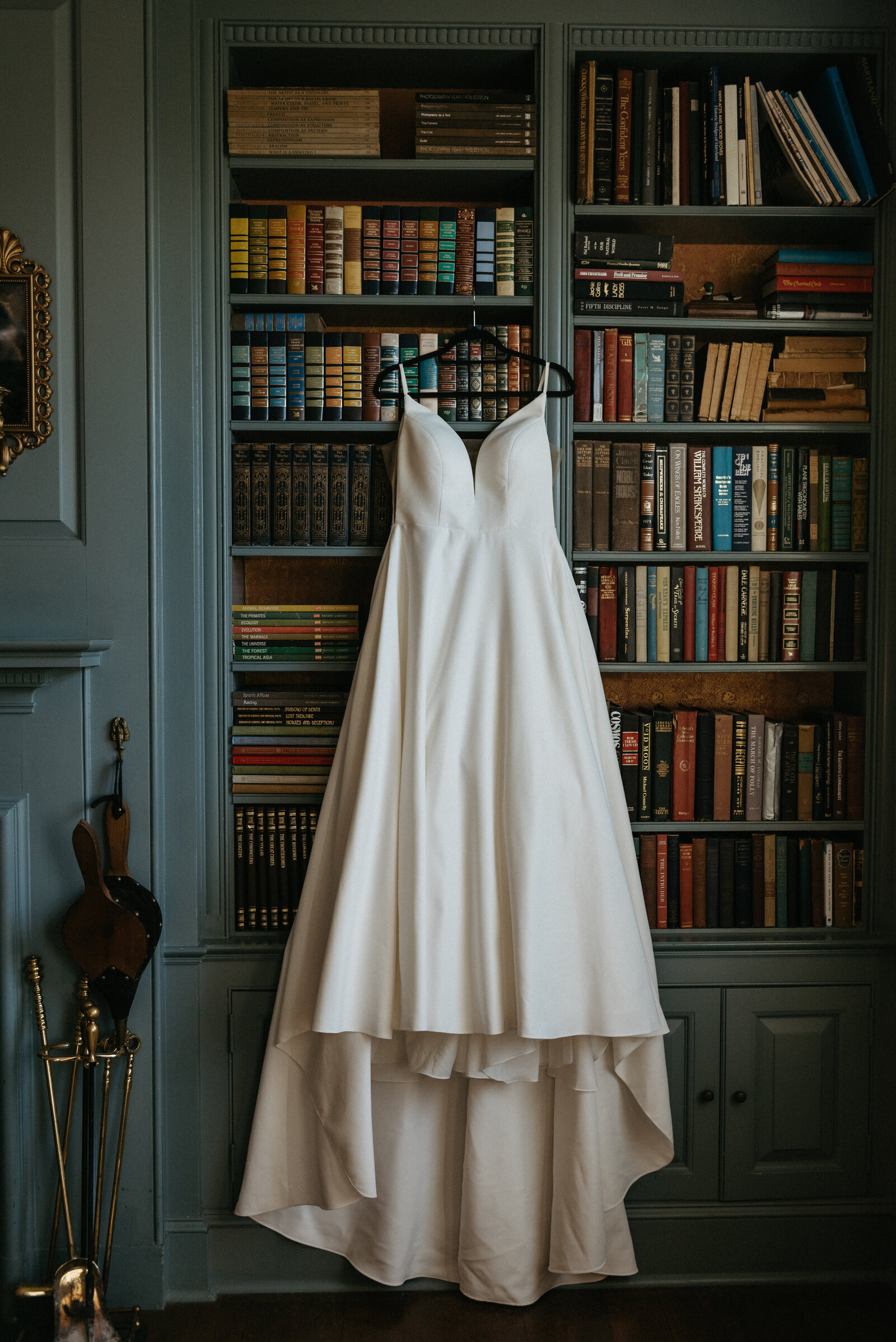 A wedding dress hangs from a shelf of books in a library