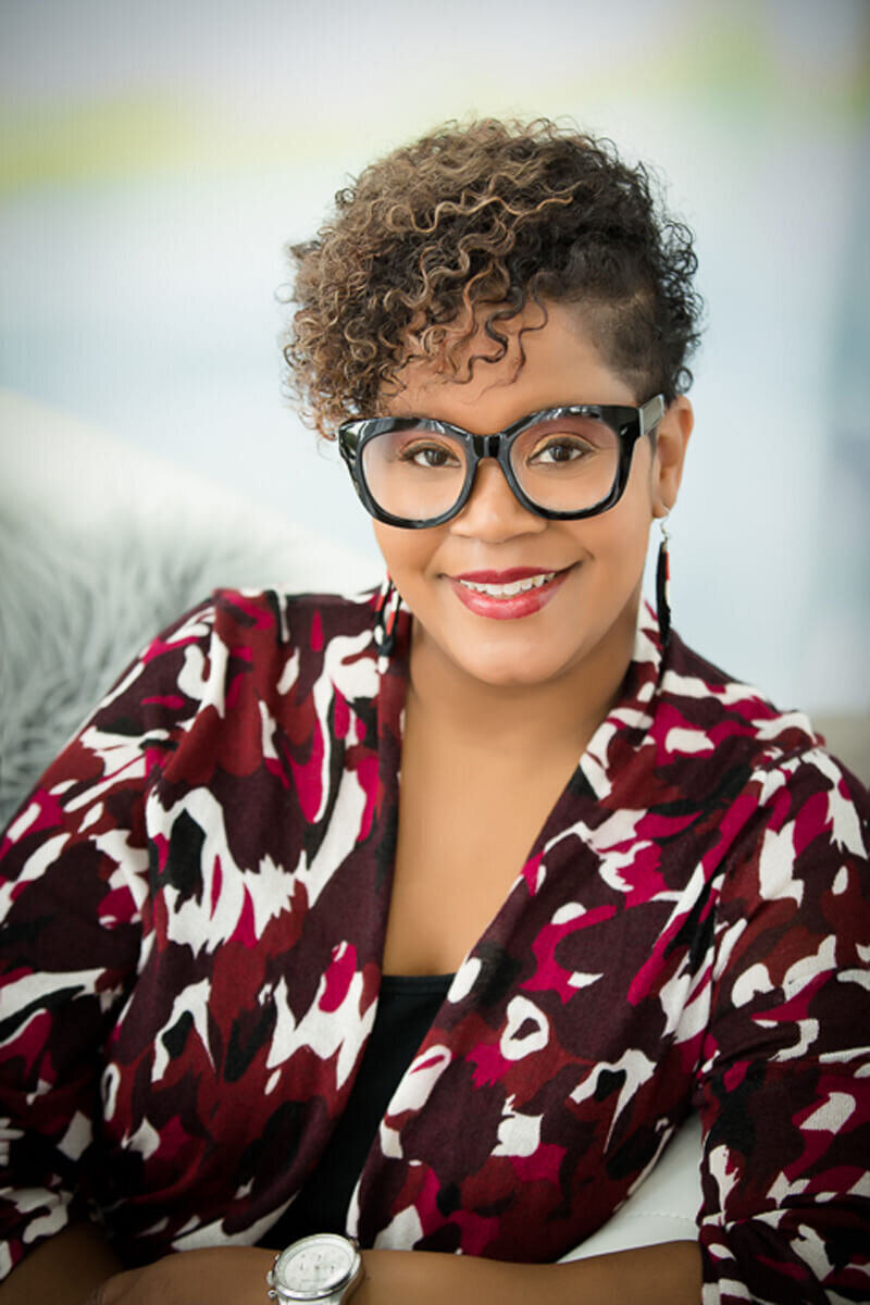 Woman in bright shirt and large-rimmed glasses smiling at the camera for headshot in Austin TX