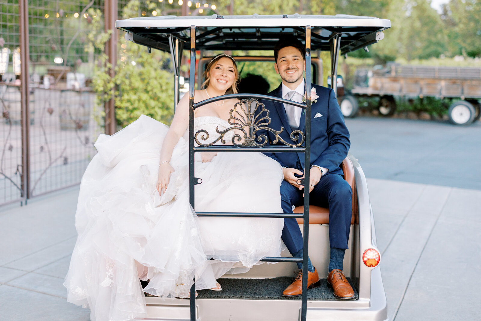 sacramento wedding photographer photographs bride and groom sitting on the back of a golf cart after their ceremony to ride to the next destination for their reception