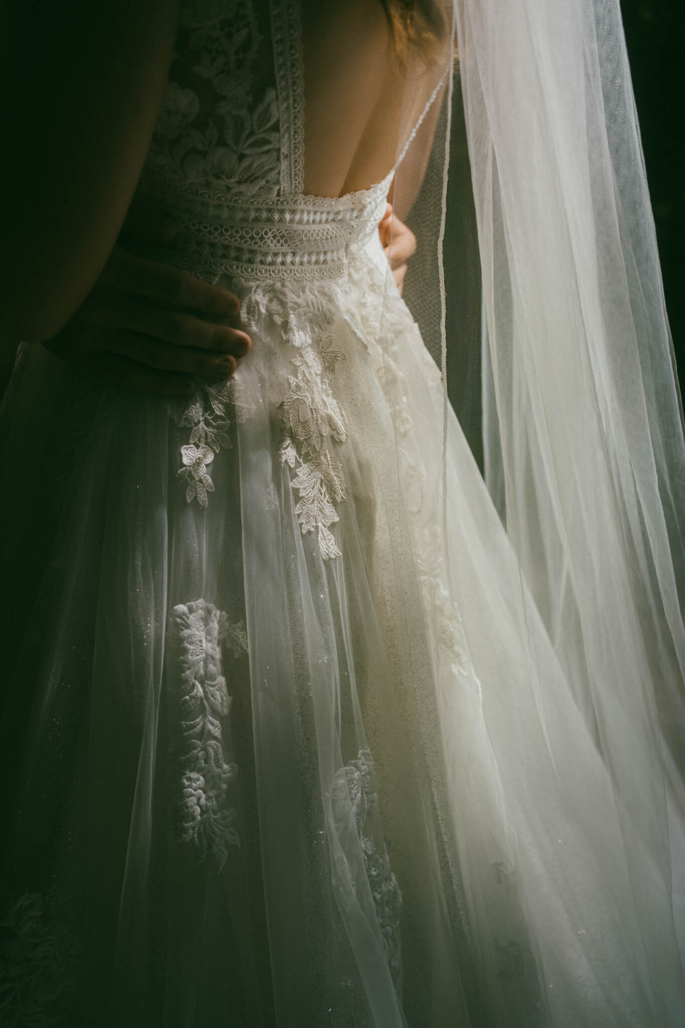A close up shot of a bride's wedding dress with the groom hugging her waist with dark and moody lighting in Georgia.