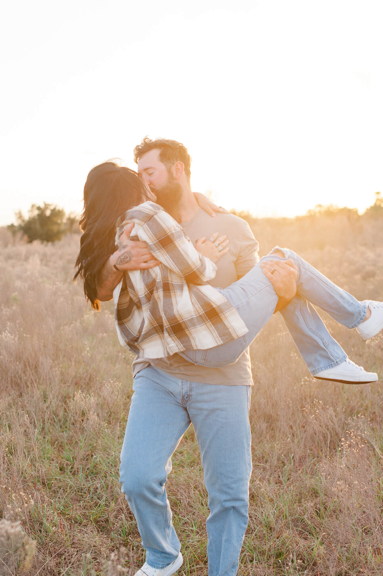 Couple kissing while husband carries wife through a tall grass pampas field