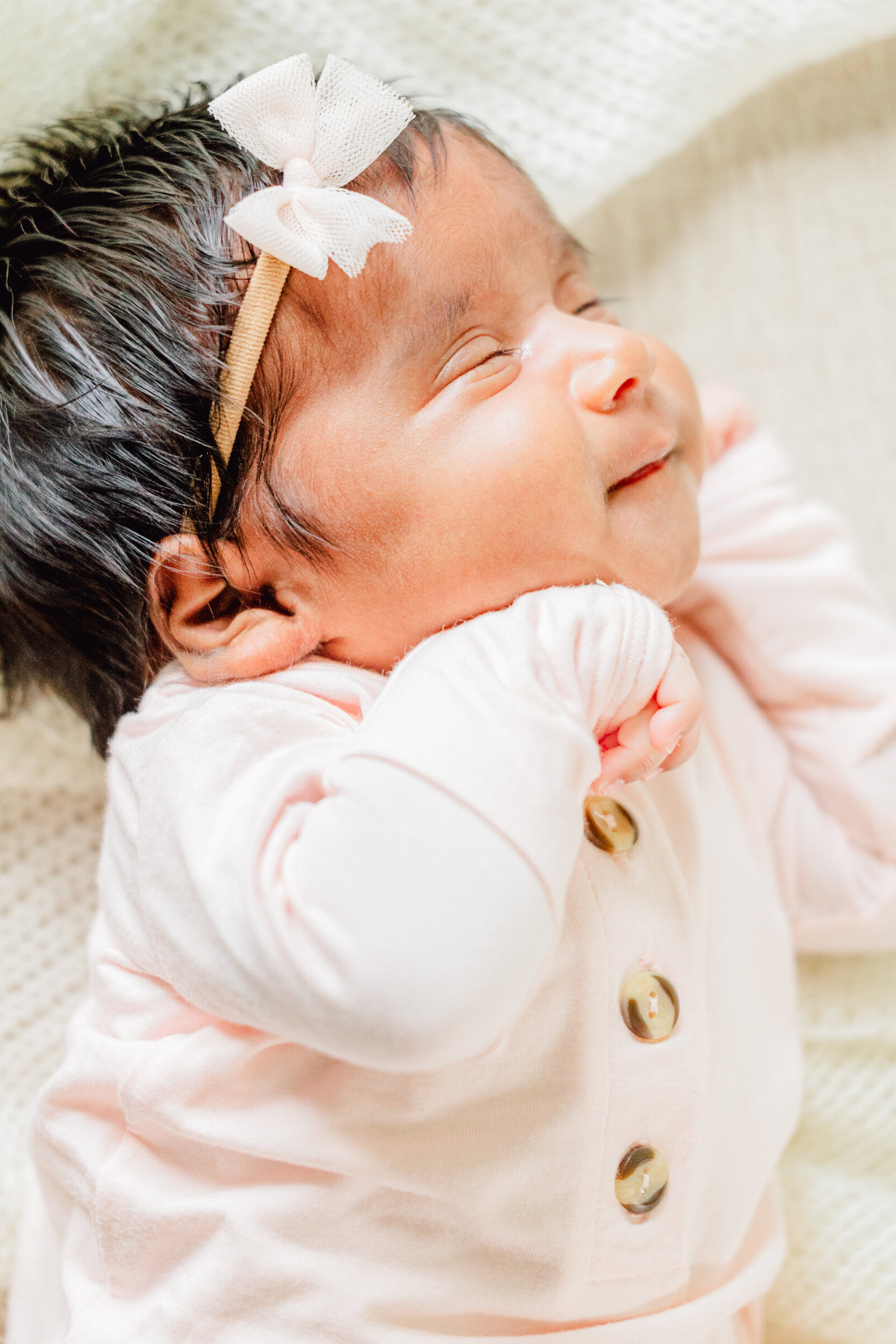 Newborn with dark hair smiles with her hand near her mouth