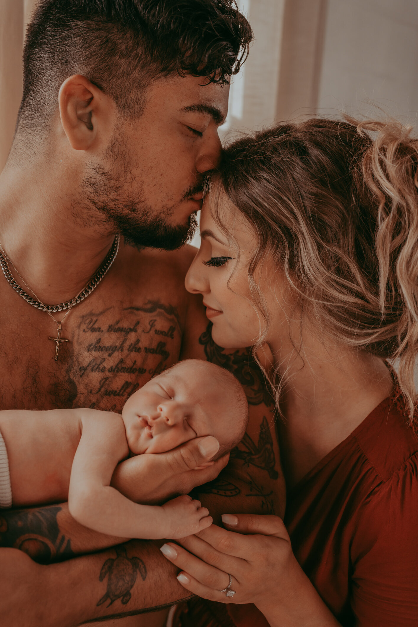 tattooed dad holds infant son while kissing wife's forehead