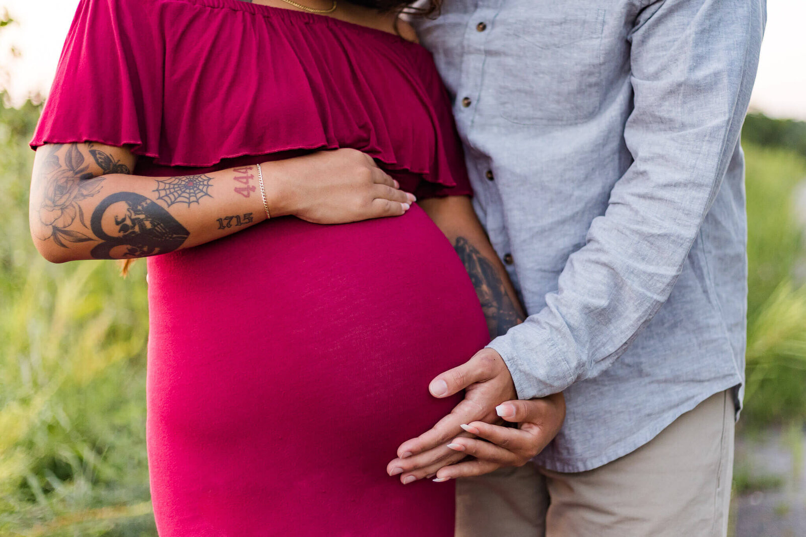 A close-up of a mom's pregnant belly with mom and dad's hands holding the bump.