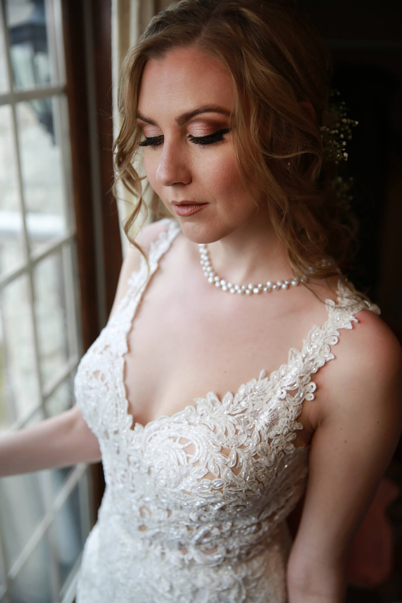 Bride portrait looking down. She is wearing classic jewellery and bridal makeup.