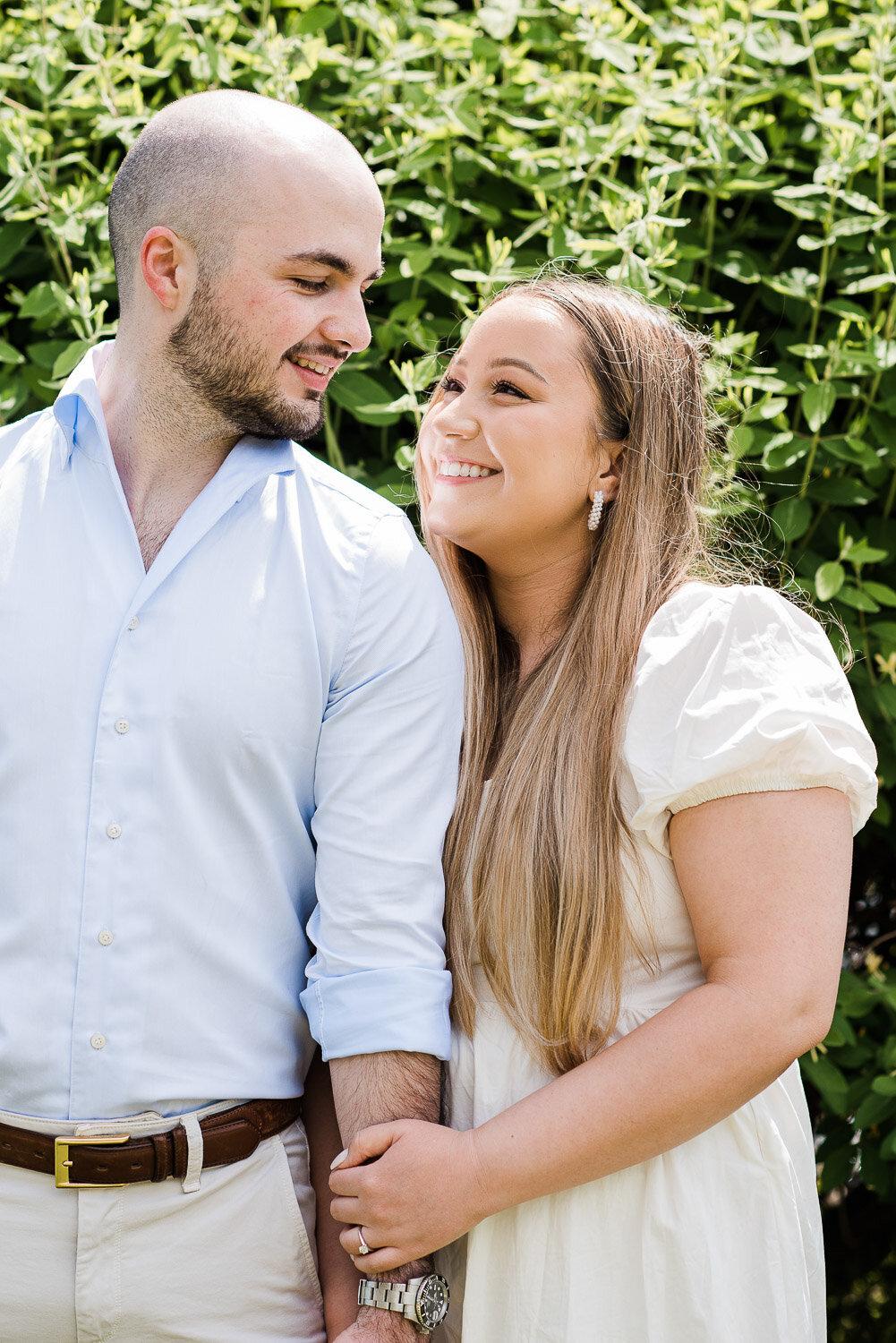 couple looking at each other holding hands in front of greenery