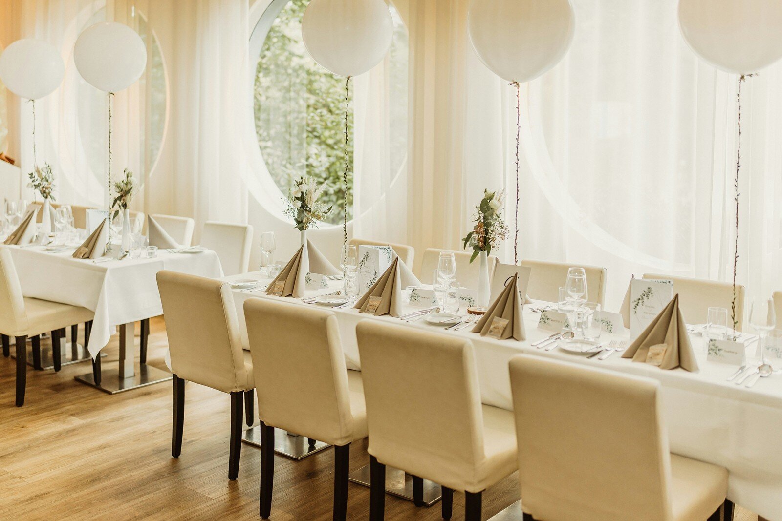 Modern reception setup with white chairs, table settings, and round balloons