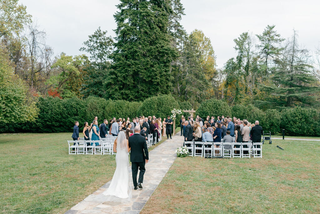 a bride being walked down the aisle by her father at an outdoor wedding