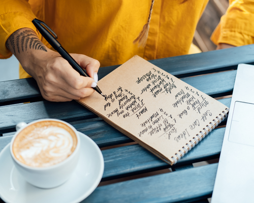 hand of a woman writing in a journal with a nature tattoo on her wrist