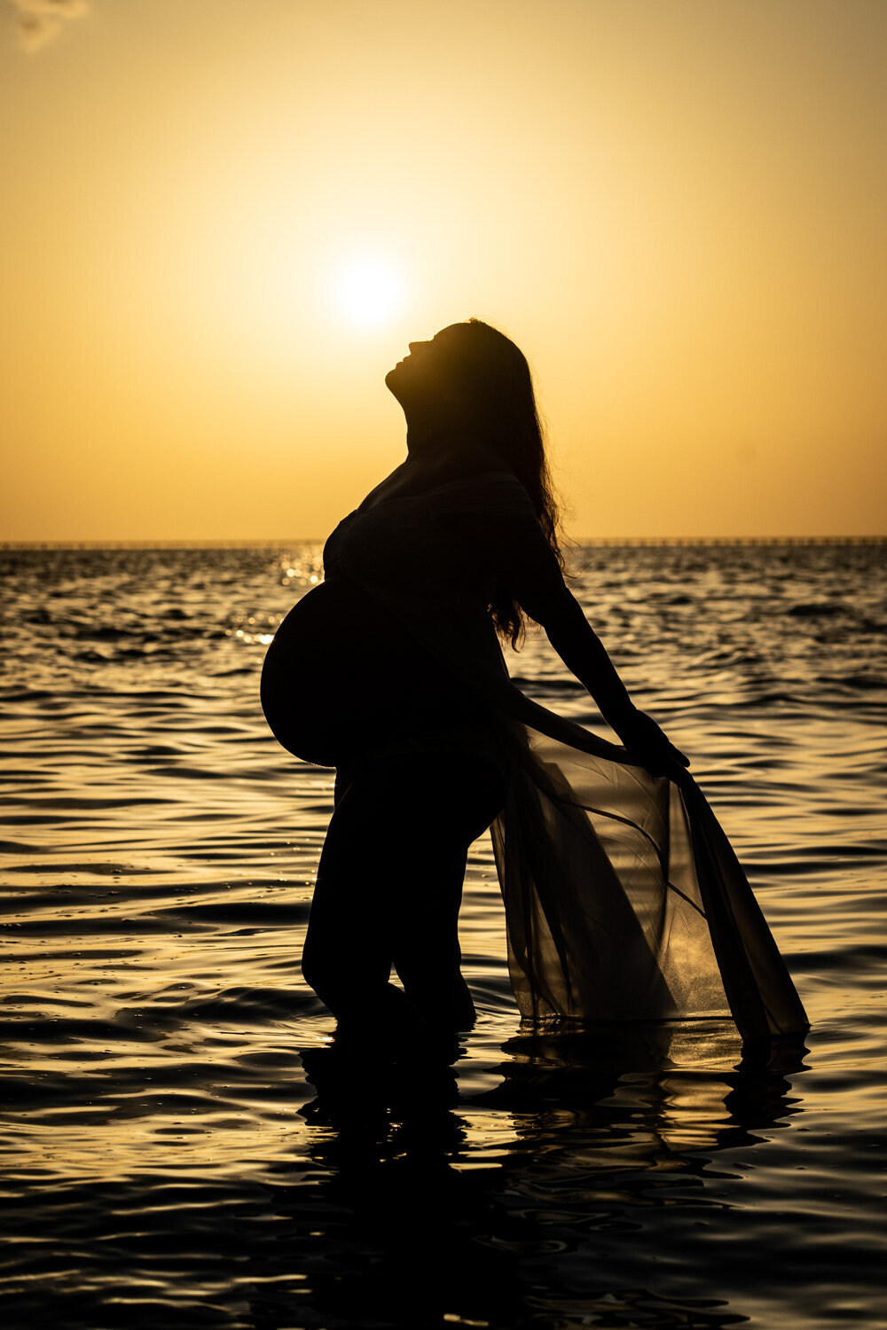 Maternity portrait, silhouette in the water with sunset in the background