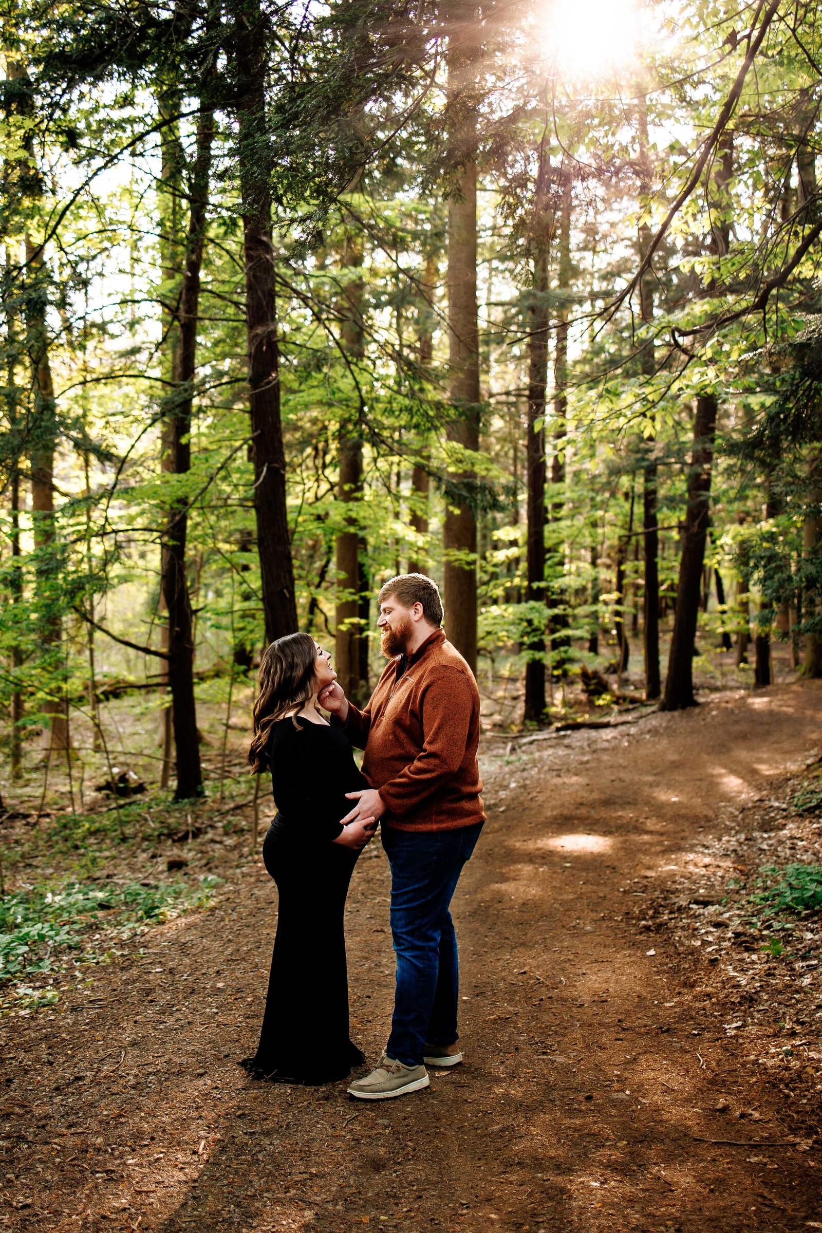 Expecting mother stands with her husband along a wooded path
