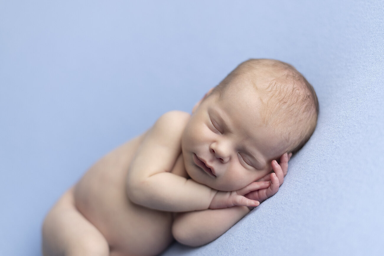 Newborn boy sleeping on blue fabric.