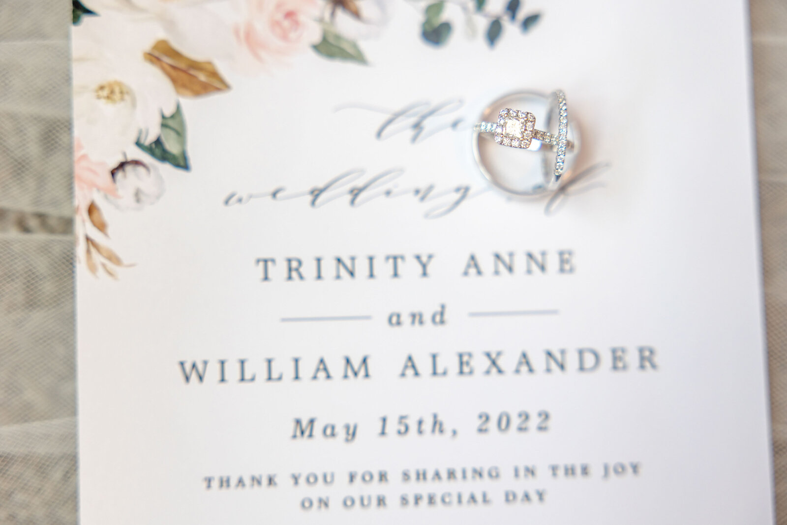 Close-up of a wedding invitation elegantly adorned with a sparkling ring, highlighting the couple's names and wedding date, beautifully captured in Oak Island, North Carolina.