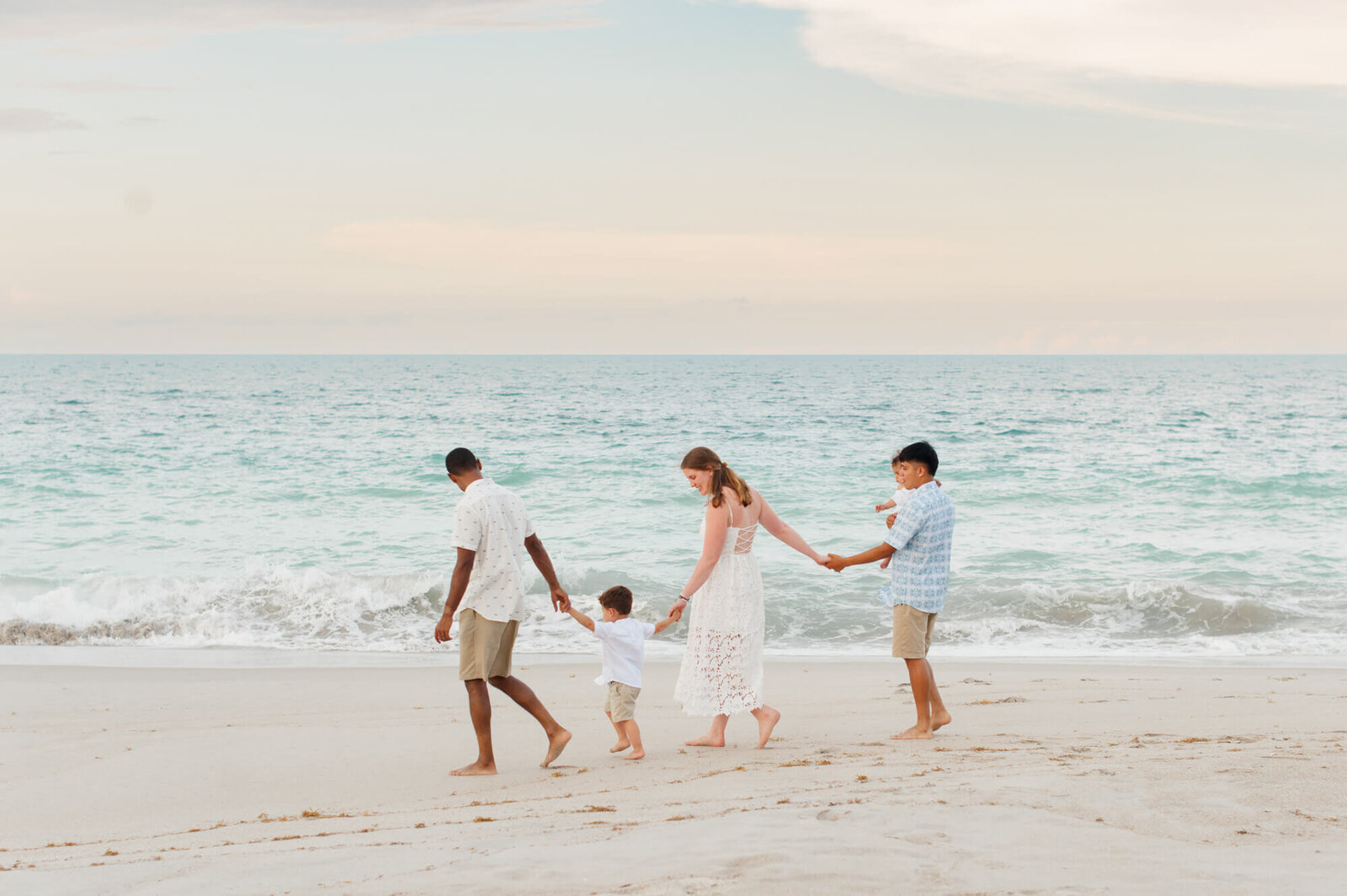 Family walking along the shoreline at the beach during their family photography session at sunset