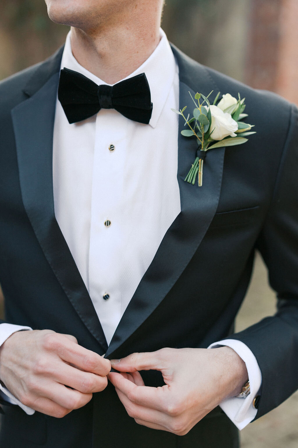 Groom wearing tuxedo with black bowtie and green boutonnière