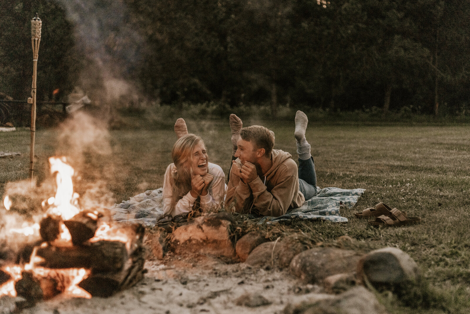 Couple laughing and laying on their elbows by a campfire