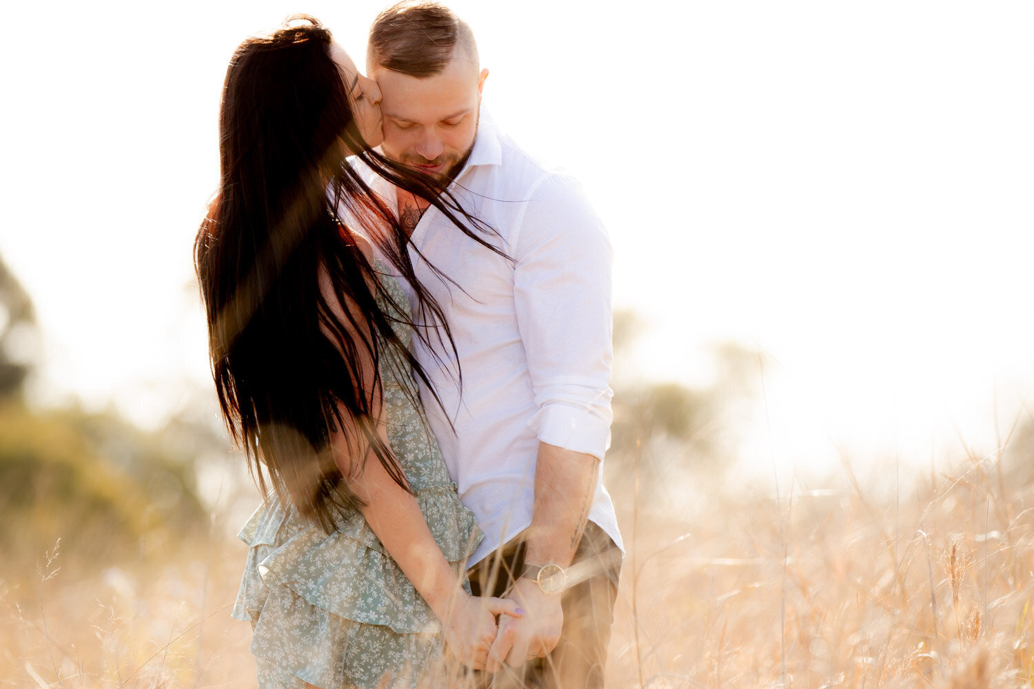 engaged couple in long grass with wind blowing