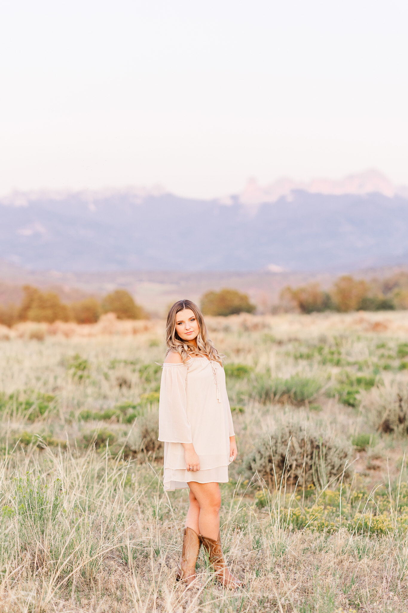 girl poses for senior pictures in open field in front of mountains