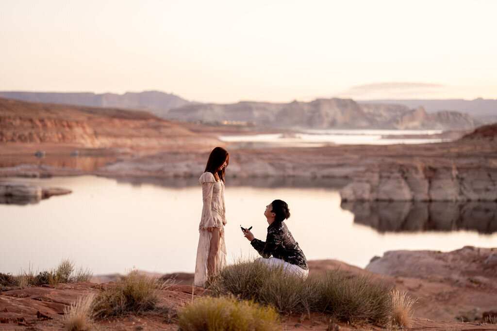 A romantic engagement proposal at sunset, with the deep orange and purple hues of the sky casting a magical glow over Lake Powell’s shoreline.