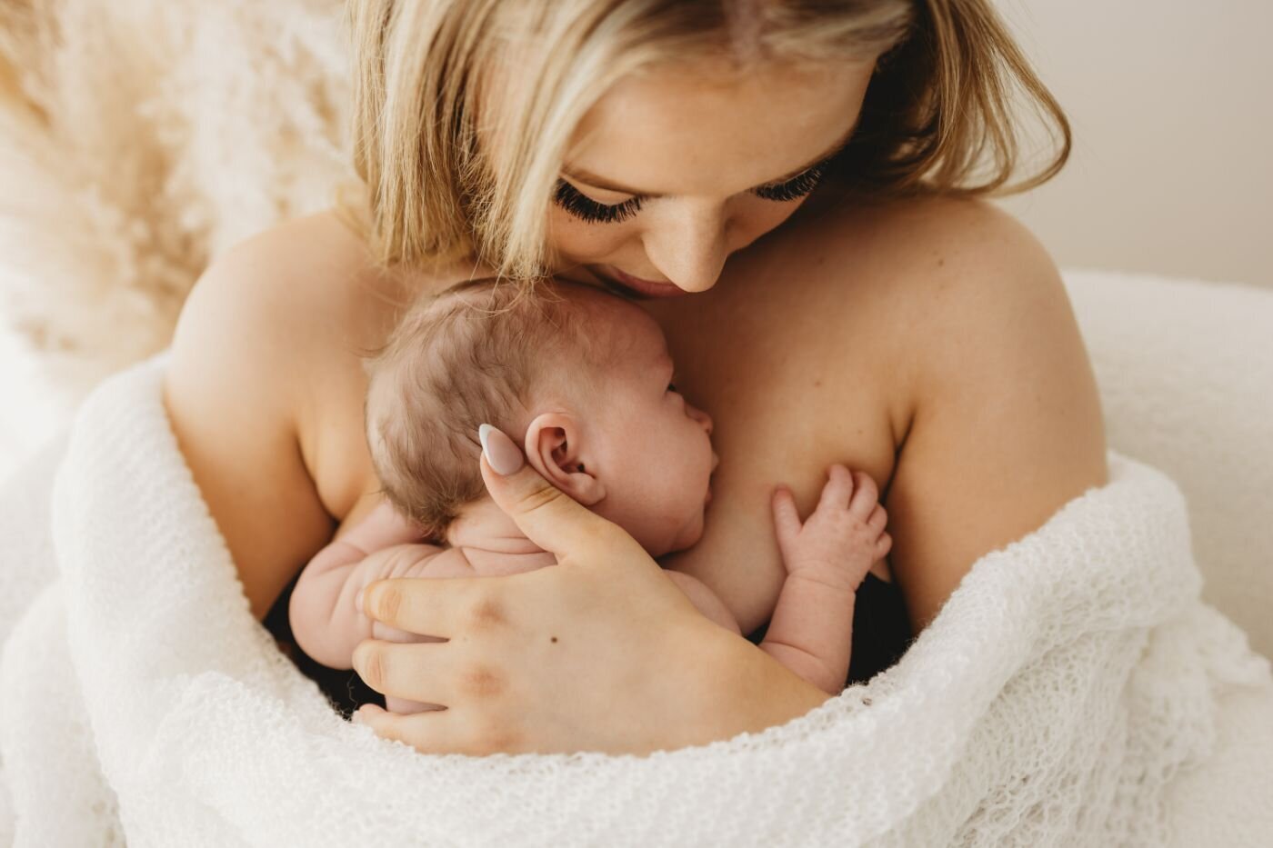 Close-up highlighting the loving embrace of a mother holding her newborn baby, who is peacefully asleep and wrapped in a soft white wrap. Ruaa Hamdan Photography, UK
