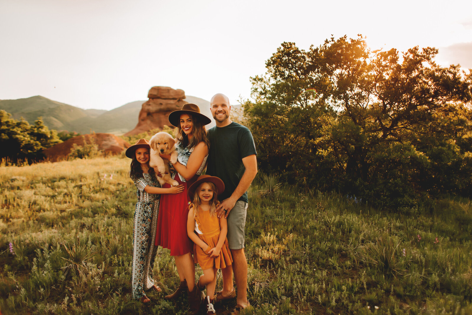 family of four posing n grassy field while holding a new puppy