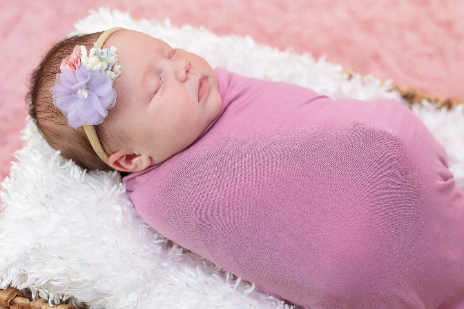 A newborn girl wrapped in pink sleeping in a basket.