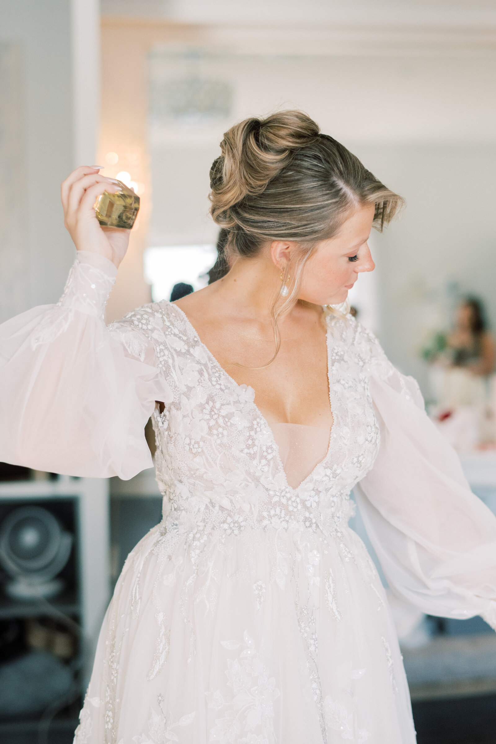 Bride in lace gown adjusting her earring, showcasing a chic, detailed bridal updo created by Promise Artistry.
