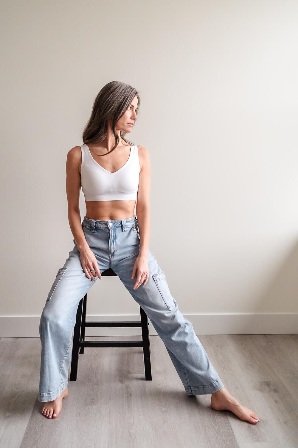 Fit businesswoman sitting on black stool in jeans and white top looking out a window