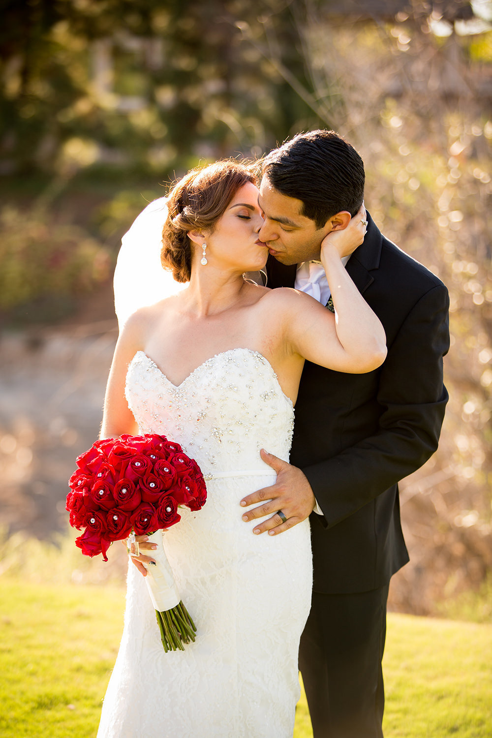 bride and groom kissing bride with red roses