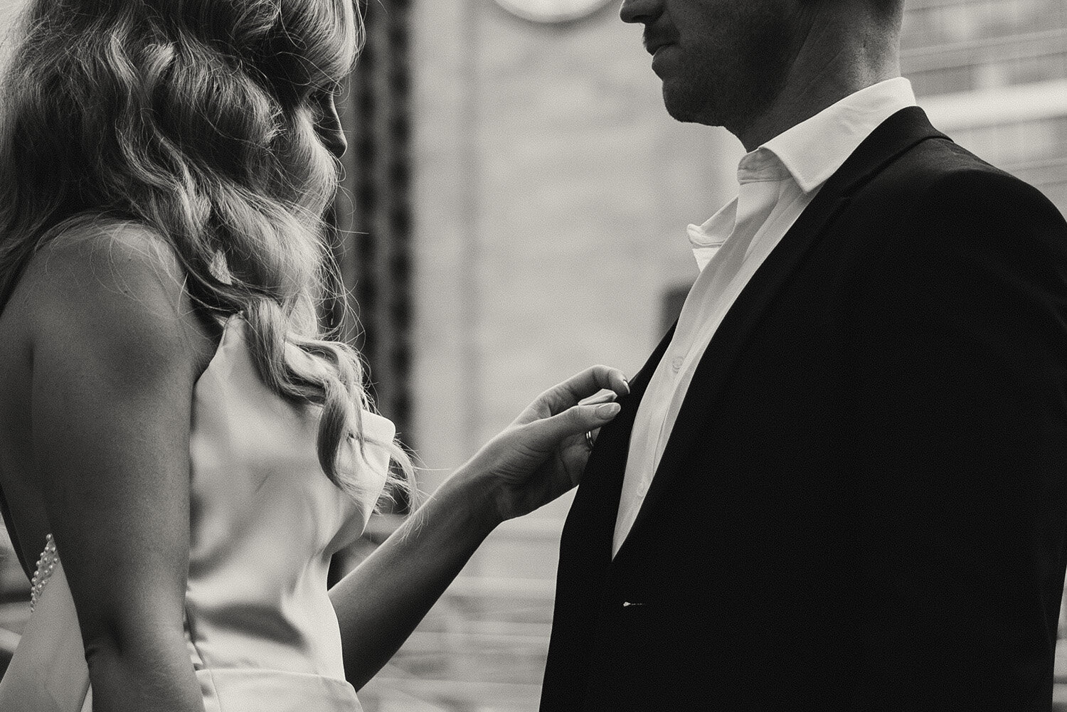 A bride adjusts a groom's jacket in an intimate black and white elopement photograph