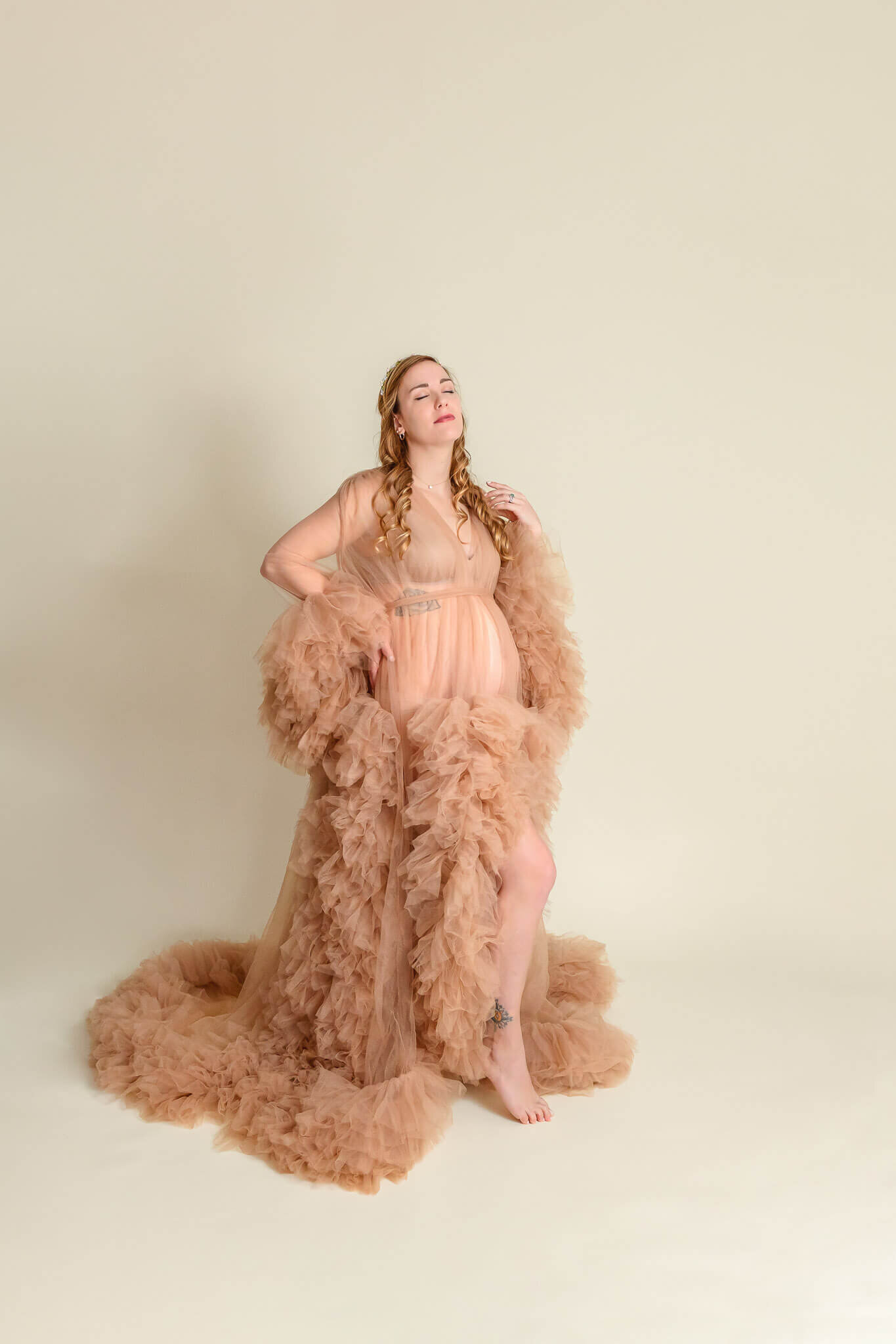 A mother-to-be wearing a tan robe on a cream backdrop.