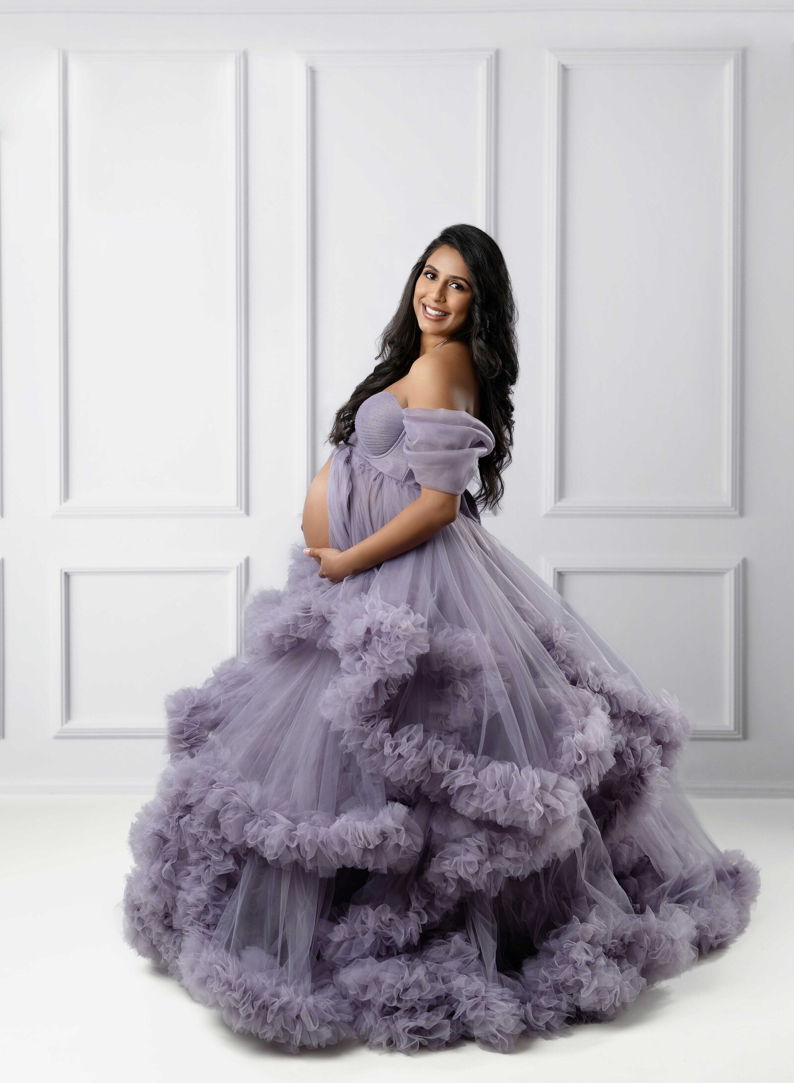 Pregnant women in purple maternity dress, spinning around as she holds baby bump. Photo taken at Atlanta Maternity photo studio.