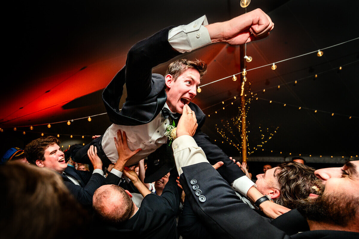 A groom is tossed into the air by his groomsmen during a lively wedding dance at the reception at Tyler Place in Highgate, Vermont, captured by Eaton Photo