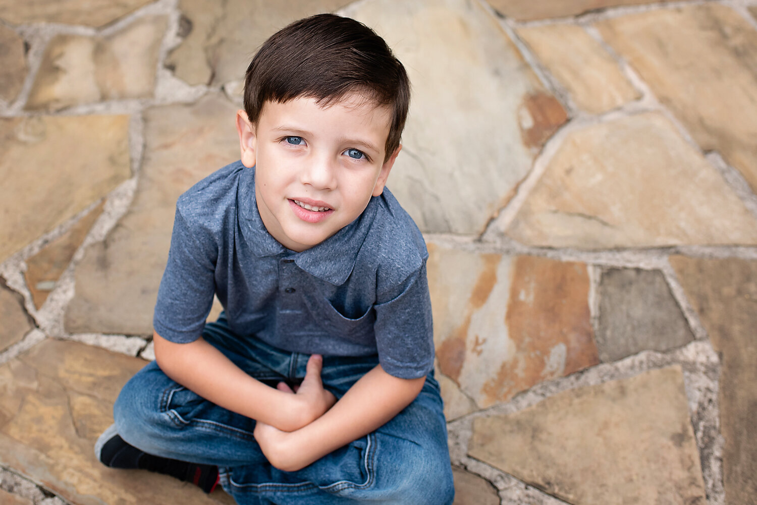 Young boy with beautiful blue eyes sitting on a stone path and gazing into the camera.