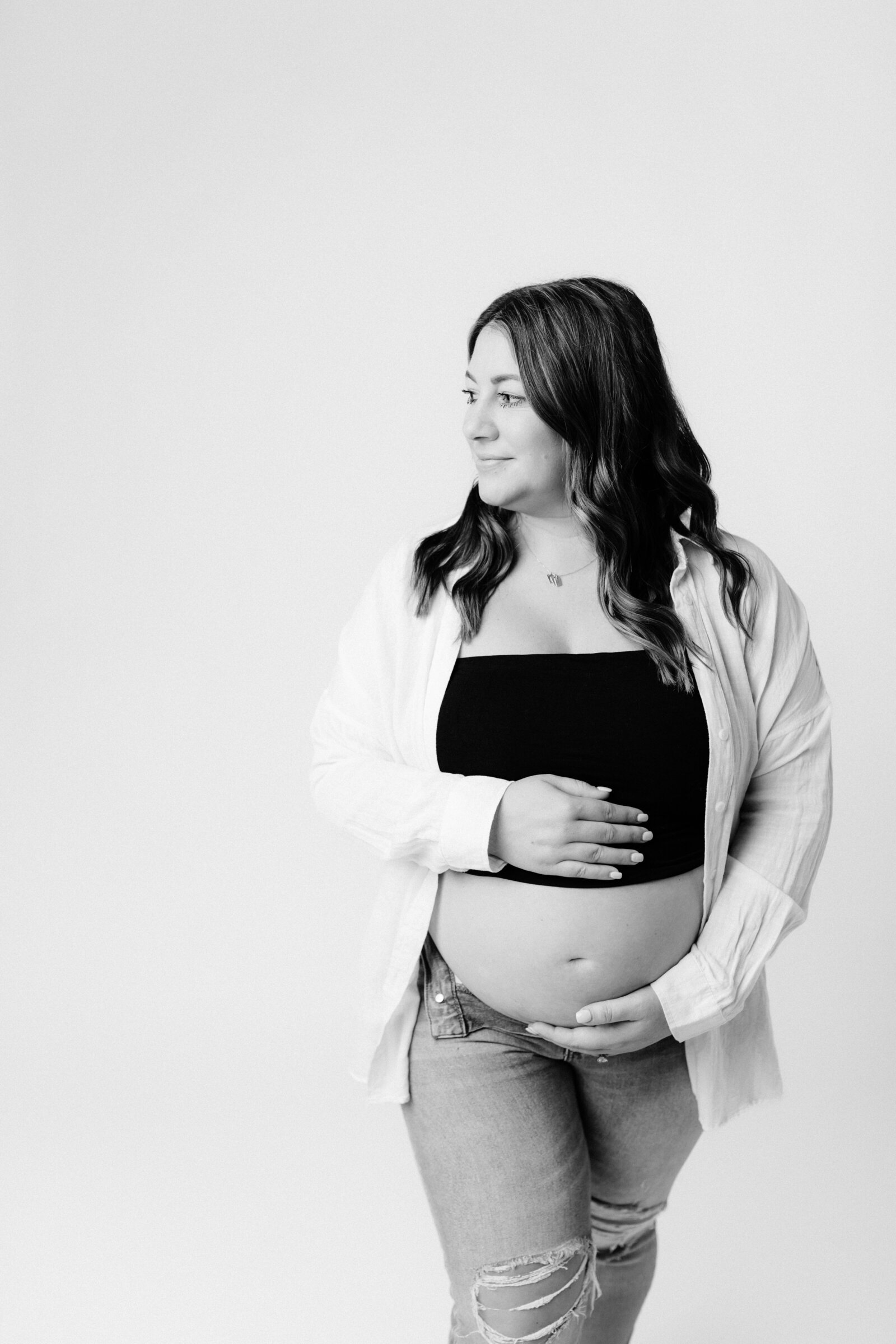 pregnant mother in sports bra and jeans holding belly for maternity photoshoot in studio